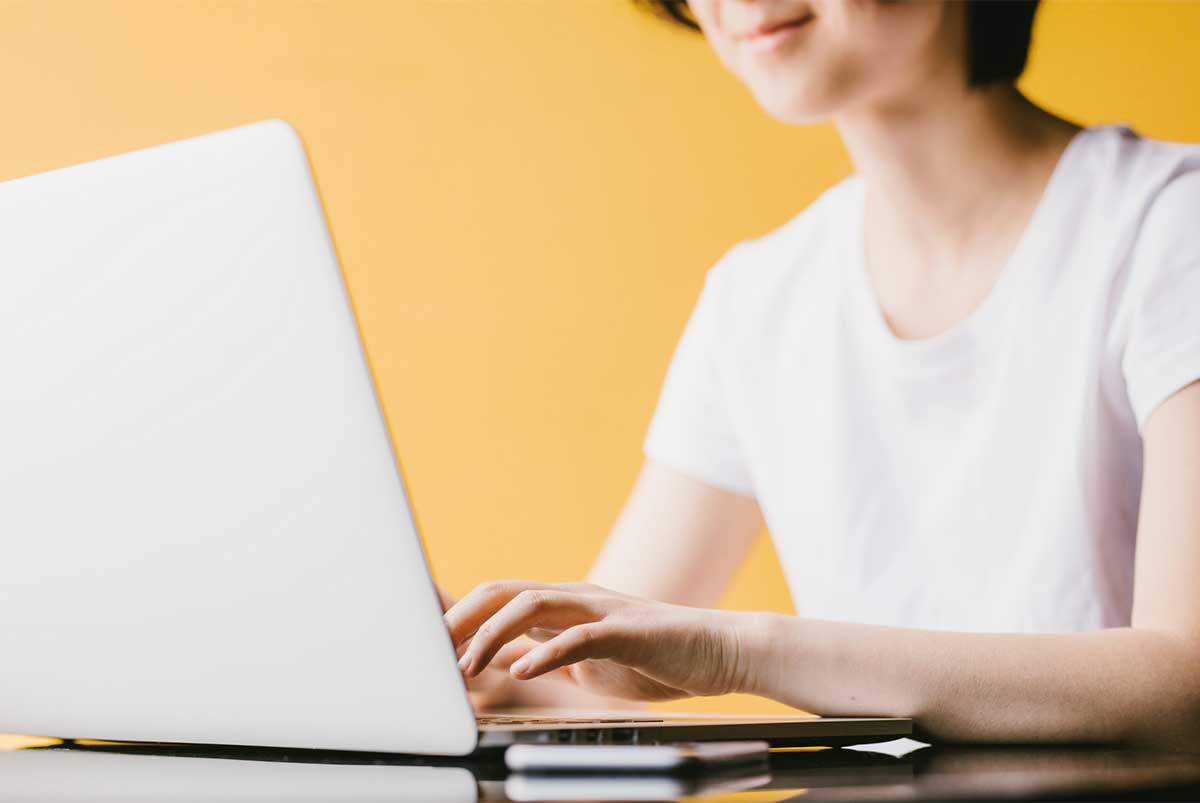 A person typing on their laptop against a yellow background