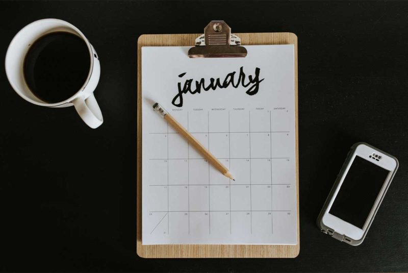 A workstation with coffee, a clipboard with a calendar and a mobile phone.