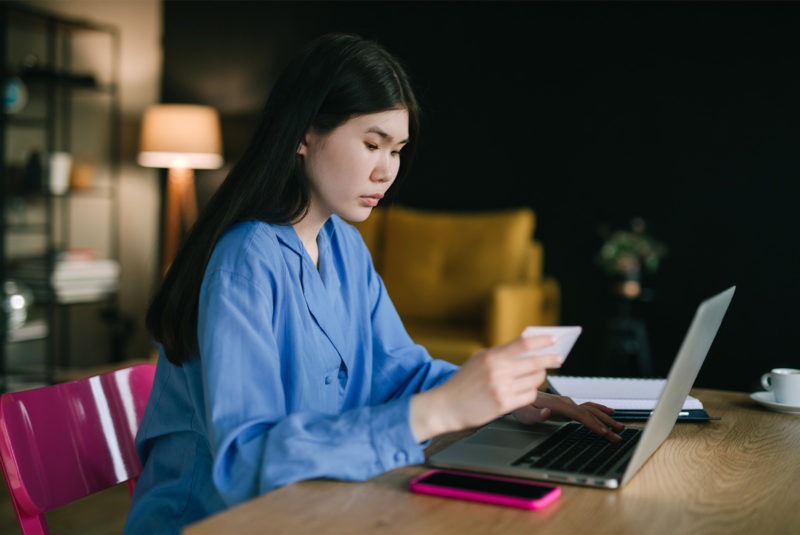 Woman looking at her credit card while sitting at her desk with her laptop