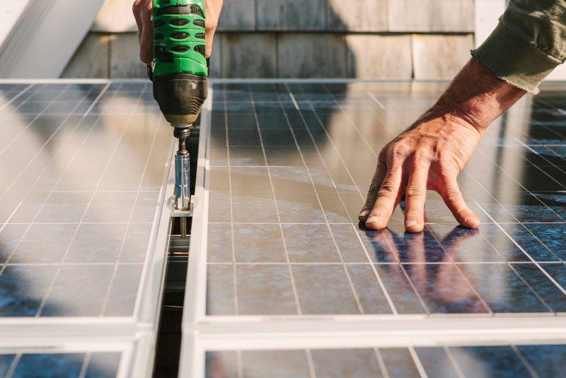 Man drilling solar panel onto roof