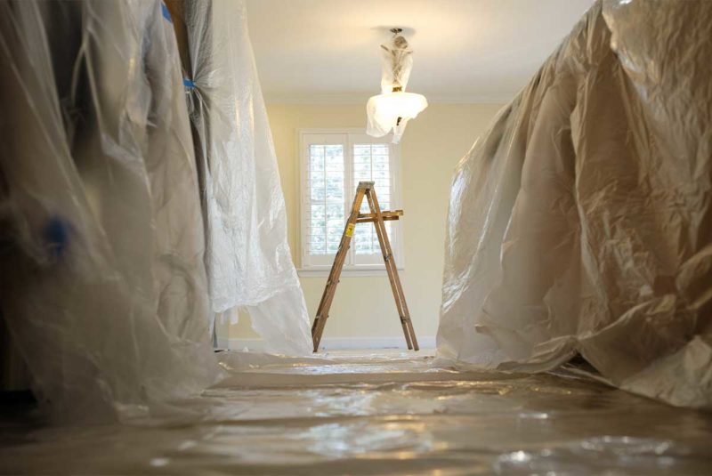 Kitchen prepared for renovation covered in plastic tarps with a ladder