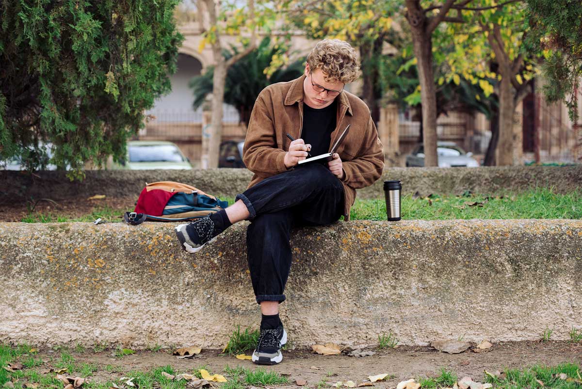 Student sitting outside writing in a notebook