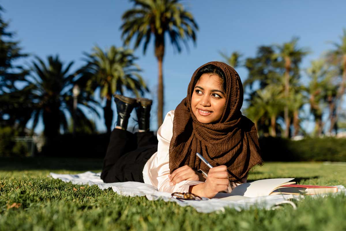 A young woman laying in the grass writing