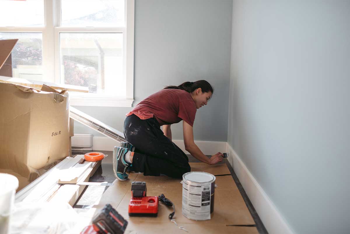 Woman painting baseboards white ina room that is being renovated