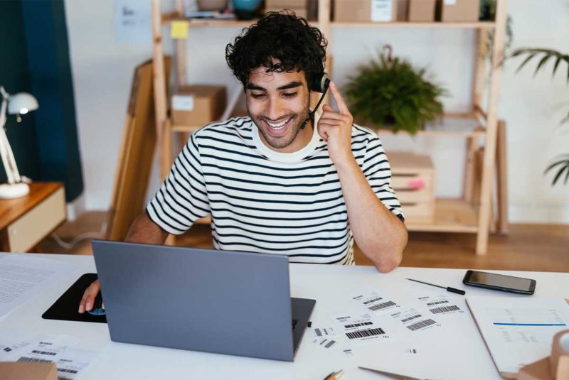 A man in a black and white striped shirt wearing headphones and sitting at a desk in front of his laptop