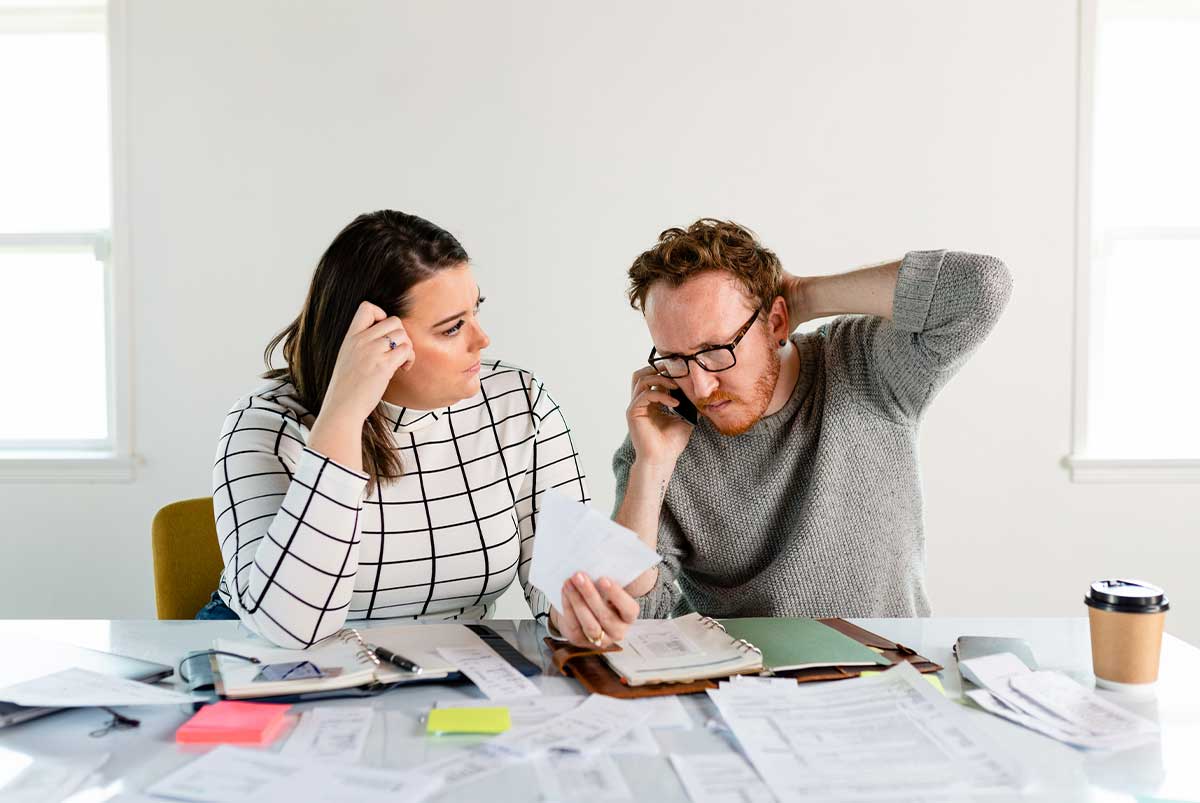 Confused-looking couple seated at a table covered with paperwork and documents