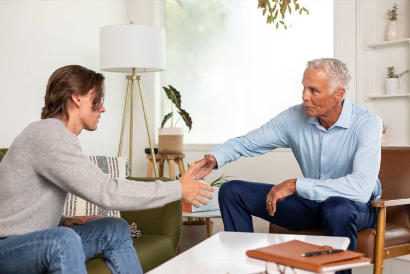 Two men about to shake hands sitting in a home