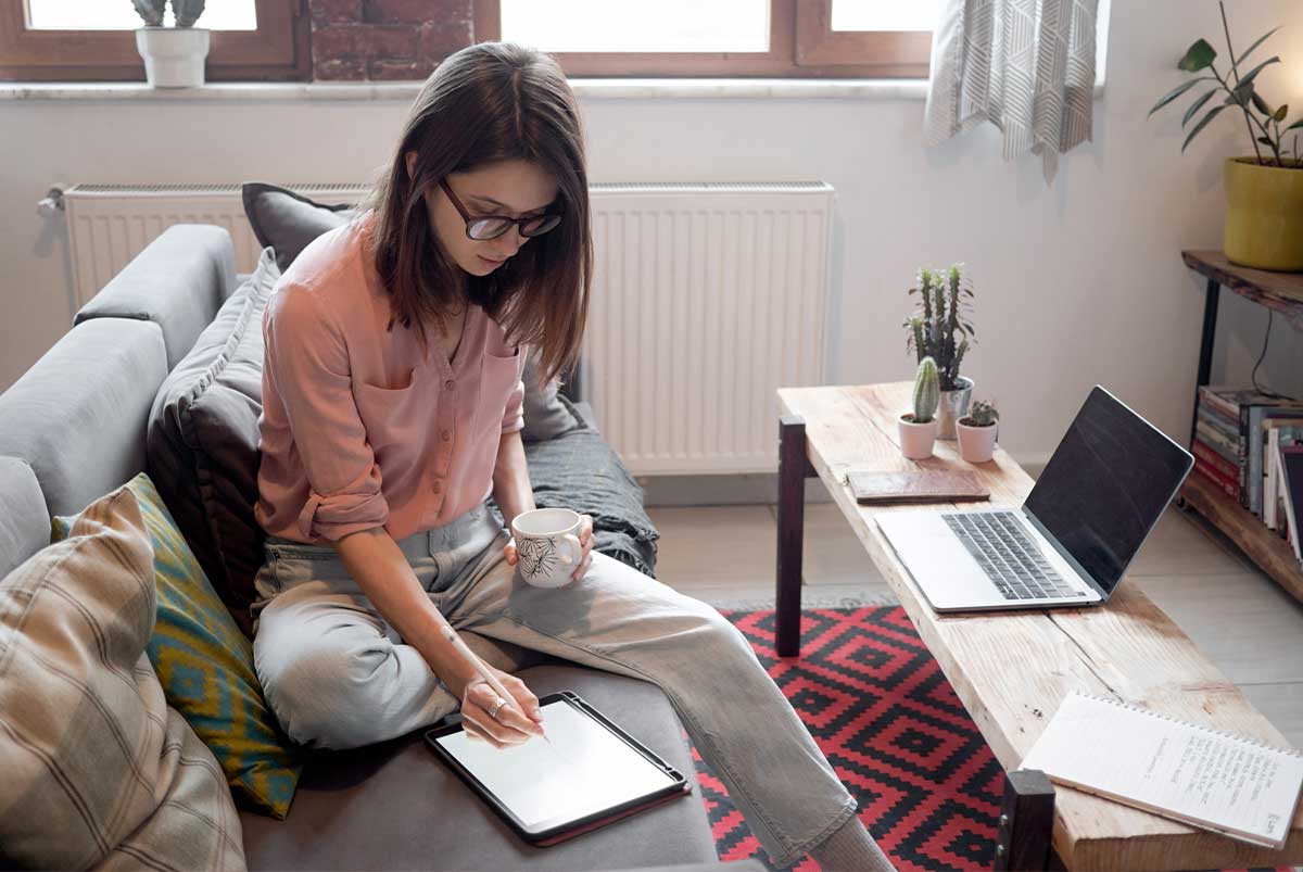 Young woman seated on a couch in a modern-looking apartment and writing in a notebook.