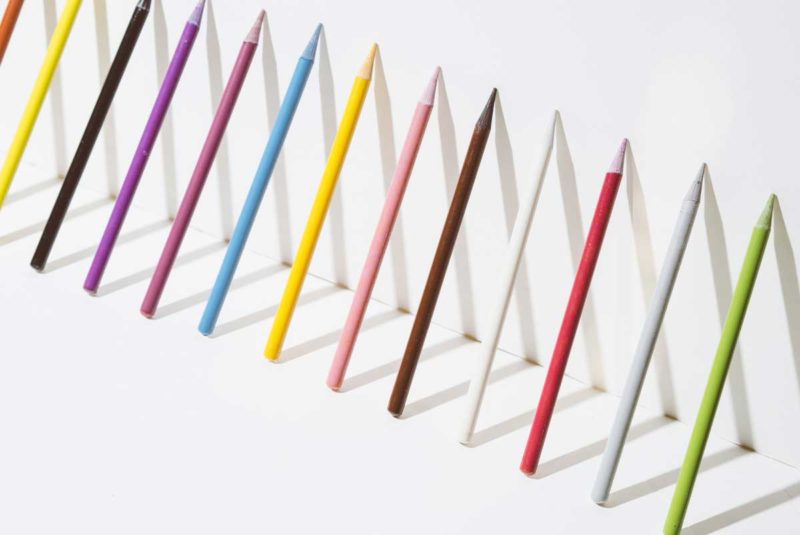 A row of colorful pencils leaning up against a white wall