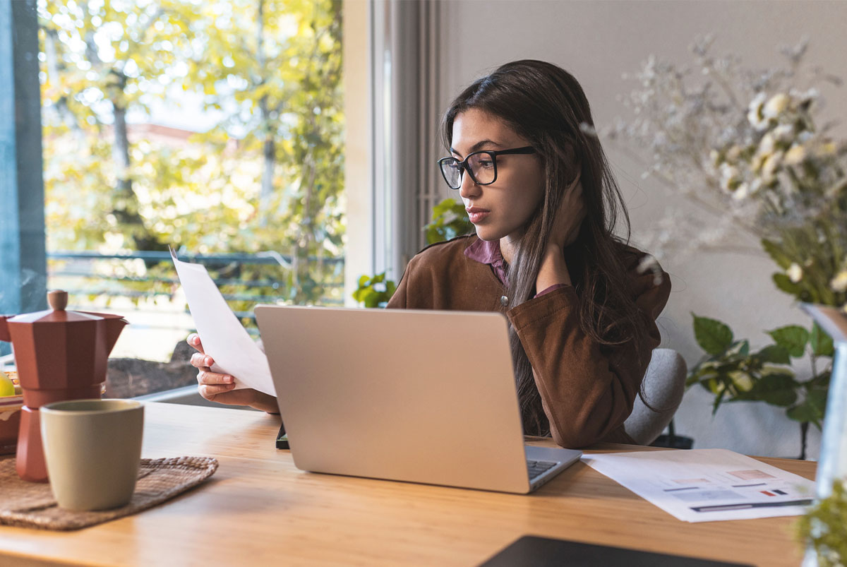 A woman sits at a laptop and reviews a copy of a verified approval letter.