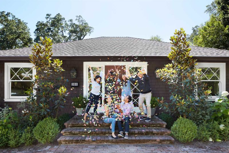 Six people on steps infront of a home, throwing confetti