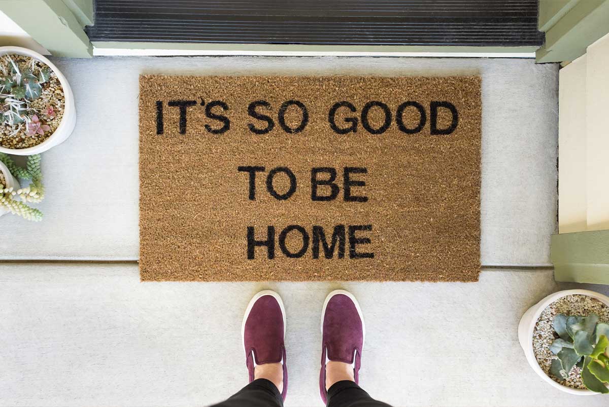 A downward view of a doormat that says, “It’s so good to be home