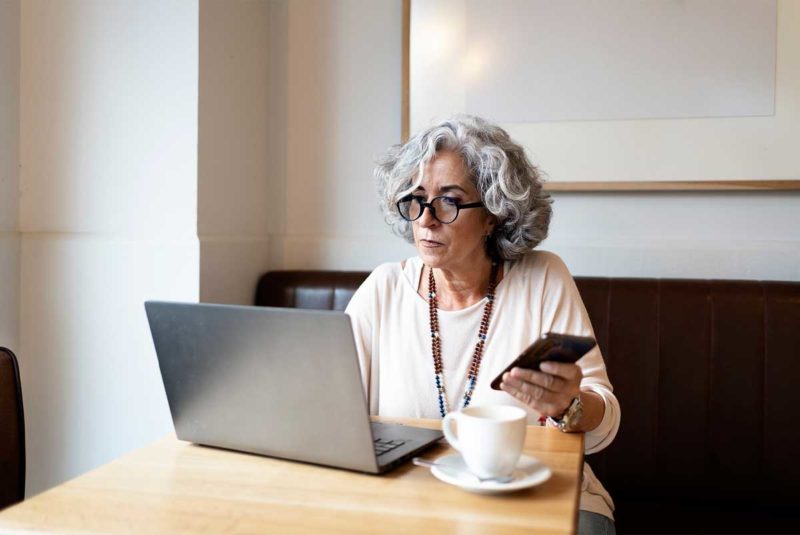 A woman on a computer holding her phone